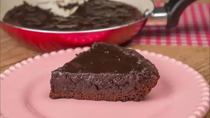 Porción de tarta de chocolate cocida en sartén, sobre plato rosa.